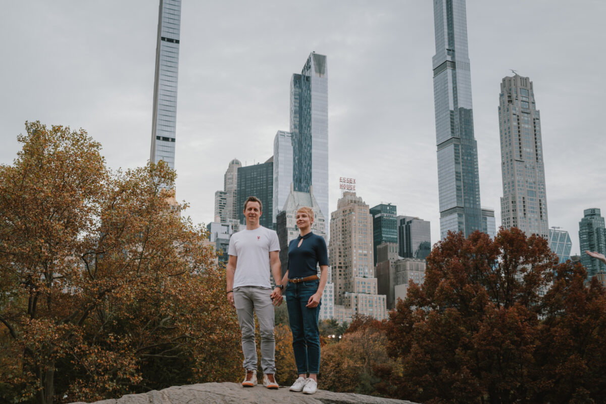 Engaged couple on a rock in Central Park with the Manhattan skyline